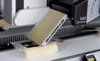 Loaf of bread positioned in a commercial bread-slicing machine, ready to be sliced in an industrial setting.