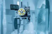 Industrial tape-reel machine with a monitor mounted on a metal frame in a cold, snowy room the equipment appears to be in a lab or Arctic facility.