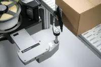 Close-up of an Evolabel labeling machine applying a label to a cardboard box on a conveyor. The reel and arm of the machine are visible alongside the box.