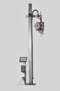 Industrial gantry-style machine mounted on a tall aluminum pillar, with wiring, a large spool, and a touchscreen control panel visible at the bottom left.
